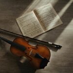 Artistic composition of a violin, sheet music, and bow in warm sunlight on a wooden floor.